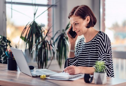 Woman talking on the smart phone and writing notes in notebook in the office