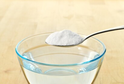 Close-up of baking soda on spoon against background of glass of water on wooden table. Bicarbonate of soda. Copy space.