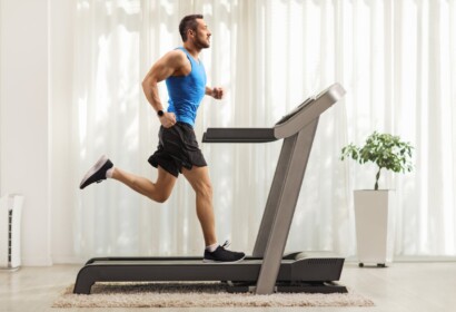 Full length profile shot of a young man running on a treadmill at home