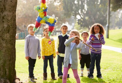 Children Hitting Pinata Hanging From A Tree At Birthday Party