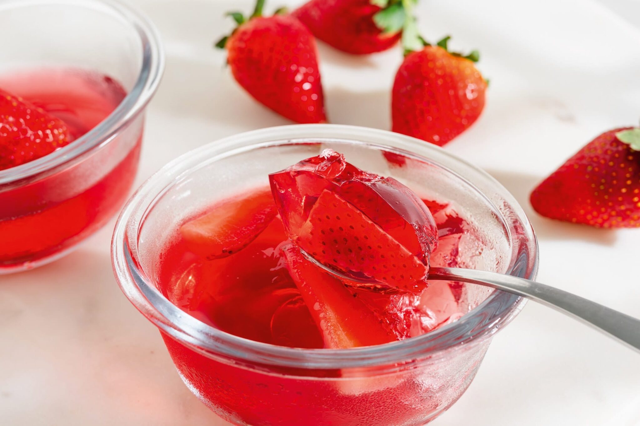 Gelatina de fresa en copes de vidre, amb una cullera que sosté un tros de gelatina amb fruita