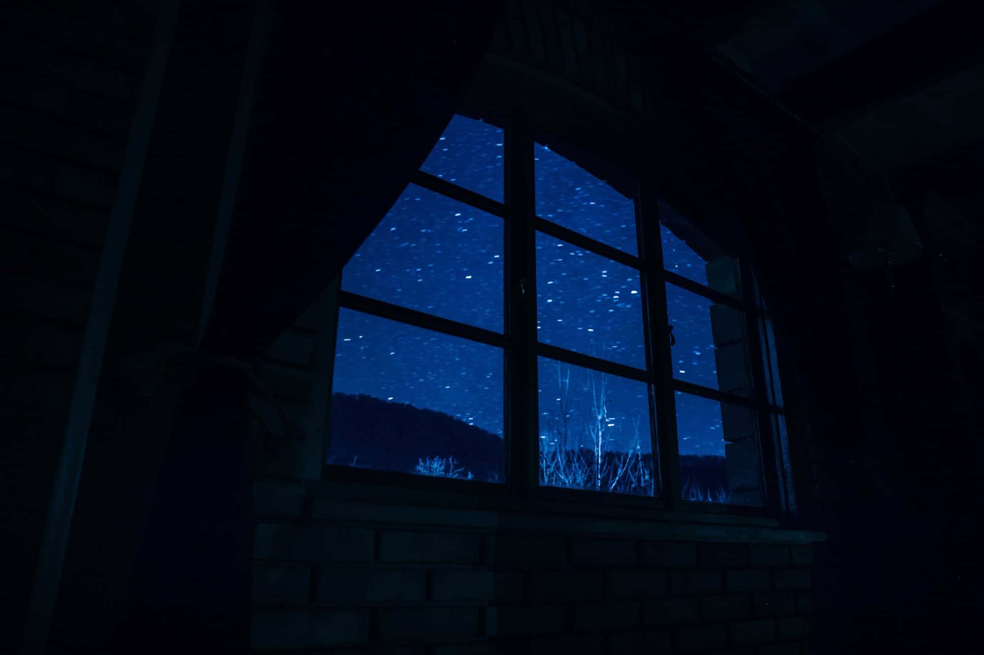 Finestra d'una habitació fosca amb un cel nocturn estrellat