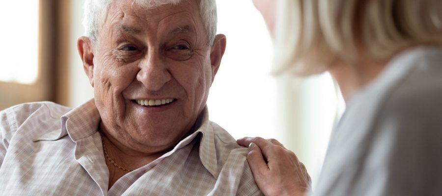 Happy older man feeling relieved after talking to supporting middle aged wife. Smiling elder male patient communicating with nurse. Female medical worker showing professional care and understanding.
