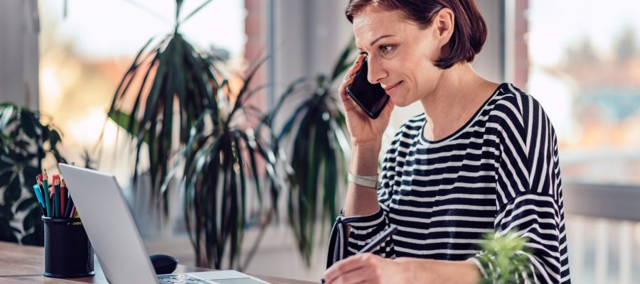 Woman talking on the smart phone and writing notes in notebook in the office