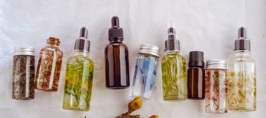 Transparent Bottles of essential oil with fresh herbs.