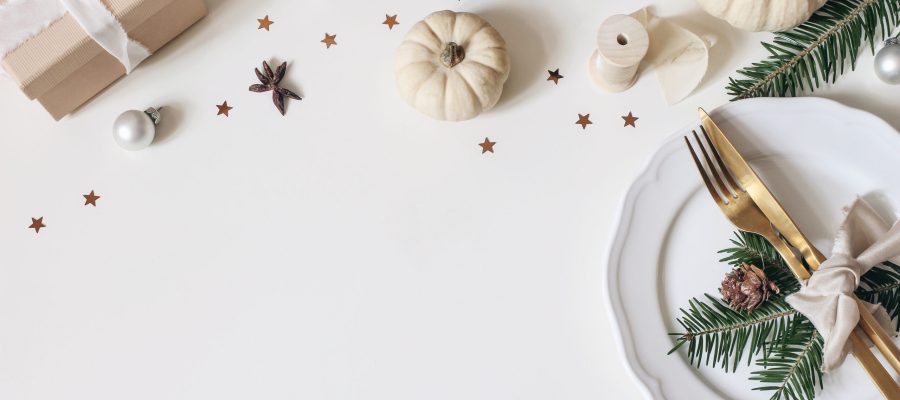 Traditional Christmas table place setting. Golden cutlery, porcelain plate, fir tree branches, gift box, pine cones and white pumkins. Christmas baubles decoration, holidays background. Flat lay, top.