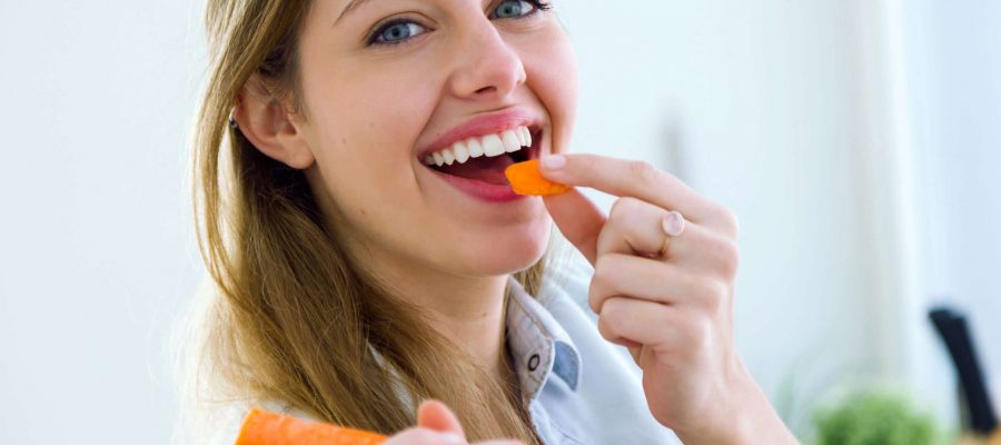 Portrait of pretty young woman eating carrot in the kitchen.