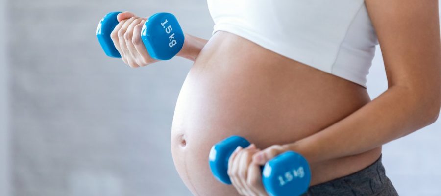 Close-up of pregnant woman doing exercise with dumbbells at home.