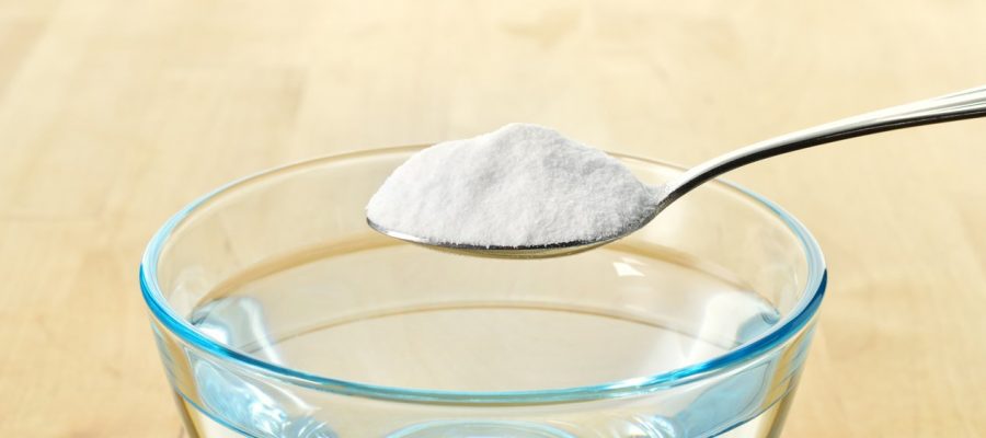 Close-up of baking soda on spoon against background of glass of water on wooden table. Bicarbonate of soda. Copy space.