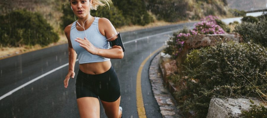 Female athlete running outdoors on highway. Beautiful young woman training running on a rainy day.