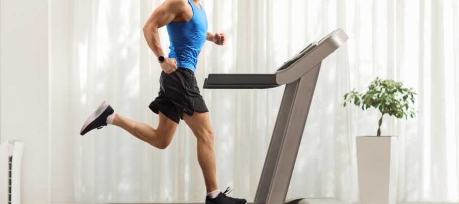 Full length profile shot of a young man running on a treadmill at home