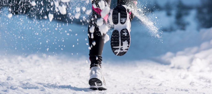 Athlete woman is running during winter training outside in cold snow weather.