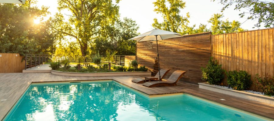 Swimming pool in modern private villa with lounge chairs, palm trees and umbrella at sunset